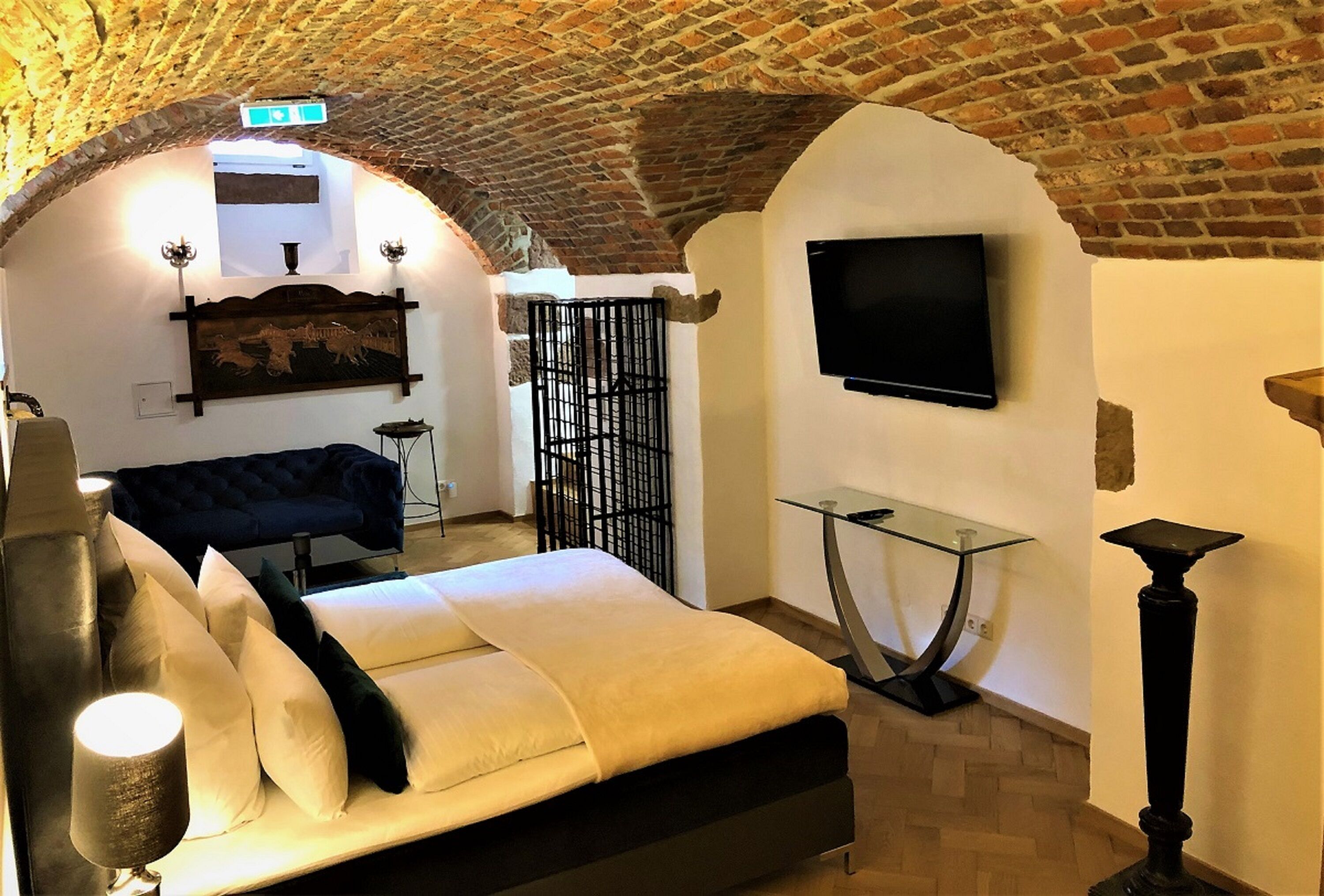 A room with a brick ceiling, a bed, a TV mounted on the wall, and a glass table.
