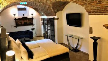 A room with a brick ceiling, a bed, a TV mounted on the wall, and a glass table.