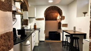 A compact kitchen with a brick archway, white cabinets, a black countertop, and a small dining area with stools. - HLH Exklusives Suite Colloseum (Freiburg im Breisgau)