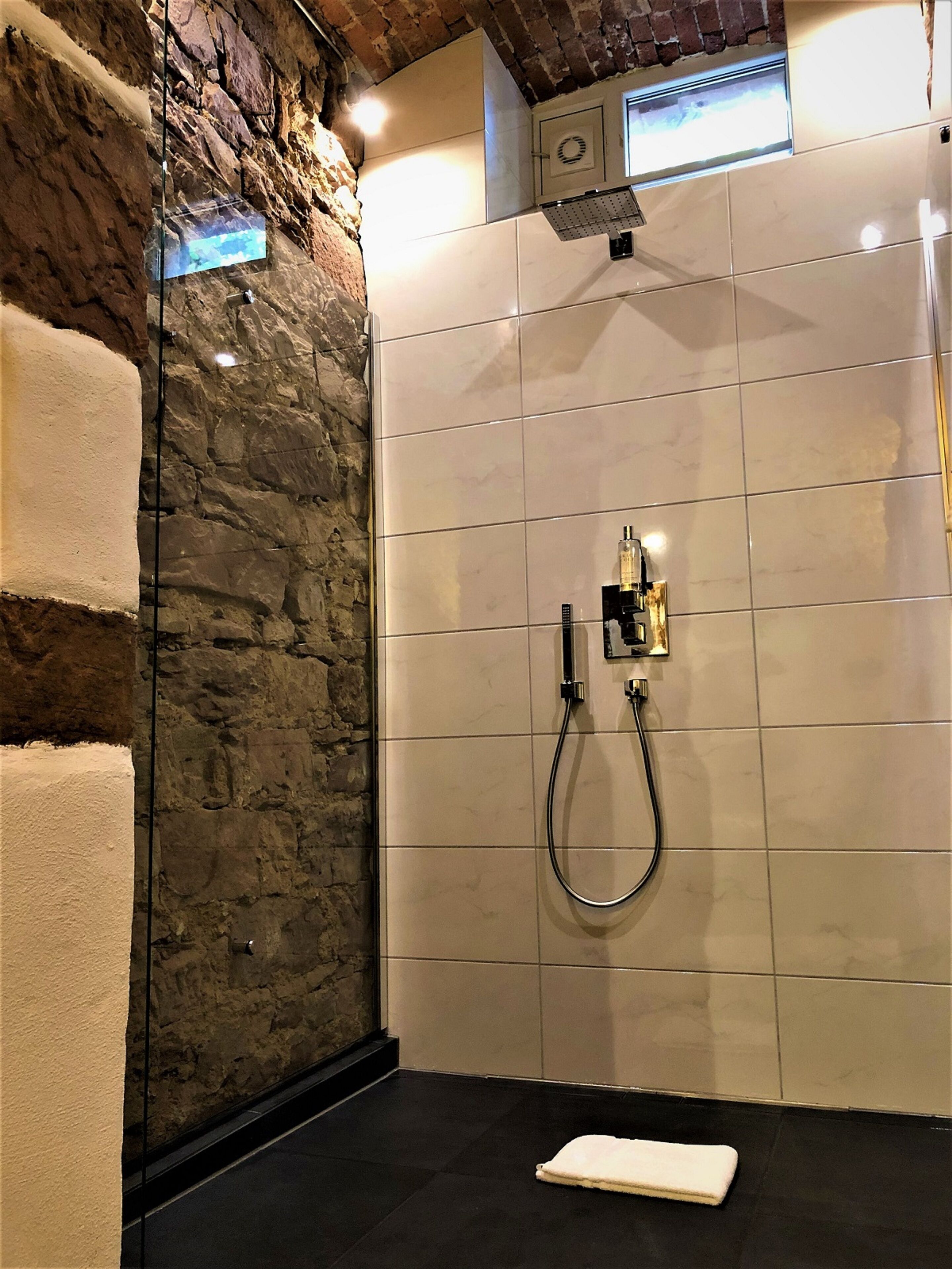 Un bagno moderno con una parete in pietra, un box doccia in vetro e un pavimento piastrellato.