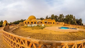 Un edificio tradicional con varias estructuras abovedadas, un patio central con piscina y una pared de ladrillo que lo rodea.