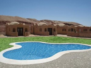 En pool omgivet af en gårdsplads med traditionel arkitektur og et bjergtag i baggrunden.