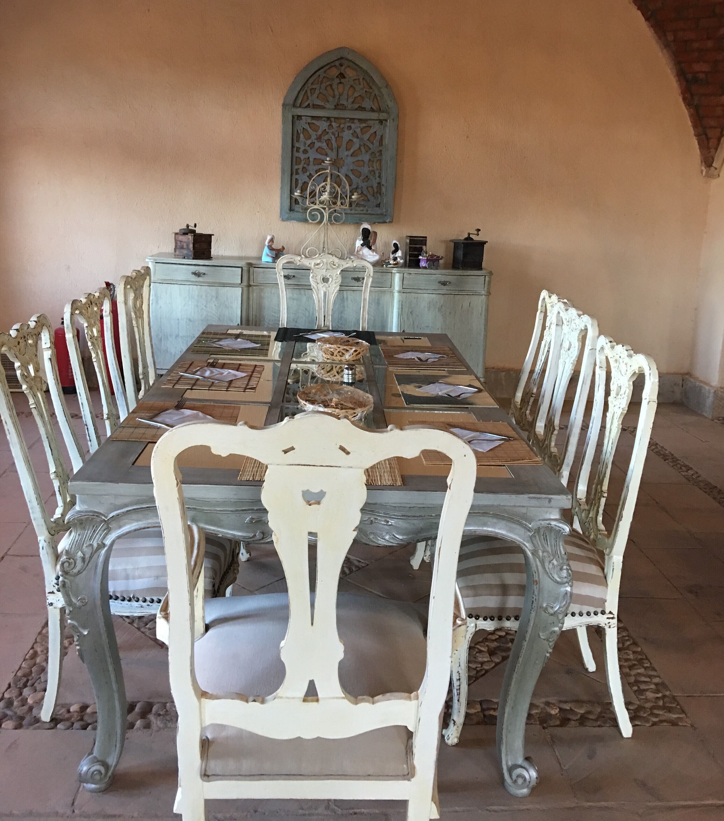 A dining room with a long table, ornate chairs, a decorative wall piece, and a vintage-style cabinet.