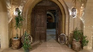 Una entrada con puerta de madera, dos faroles y plantas en macetas.