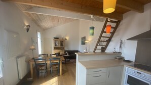 A spacious kitchen with wooden flooring, a central island with a stove, and a dining area with chairs and a table. - Charming Renovated Home Near Beach with Garden & BBQ, Sleeps 4+1 (Fouras)