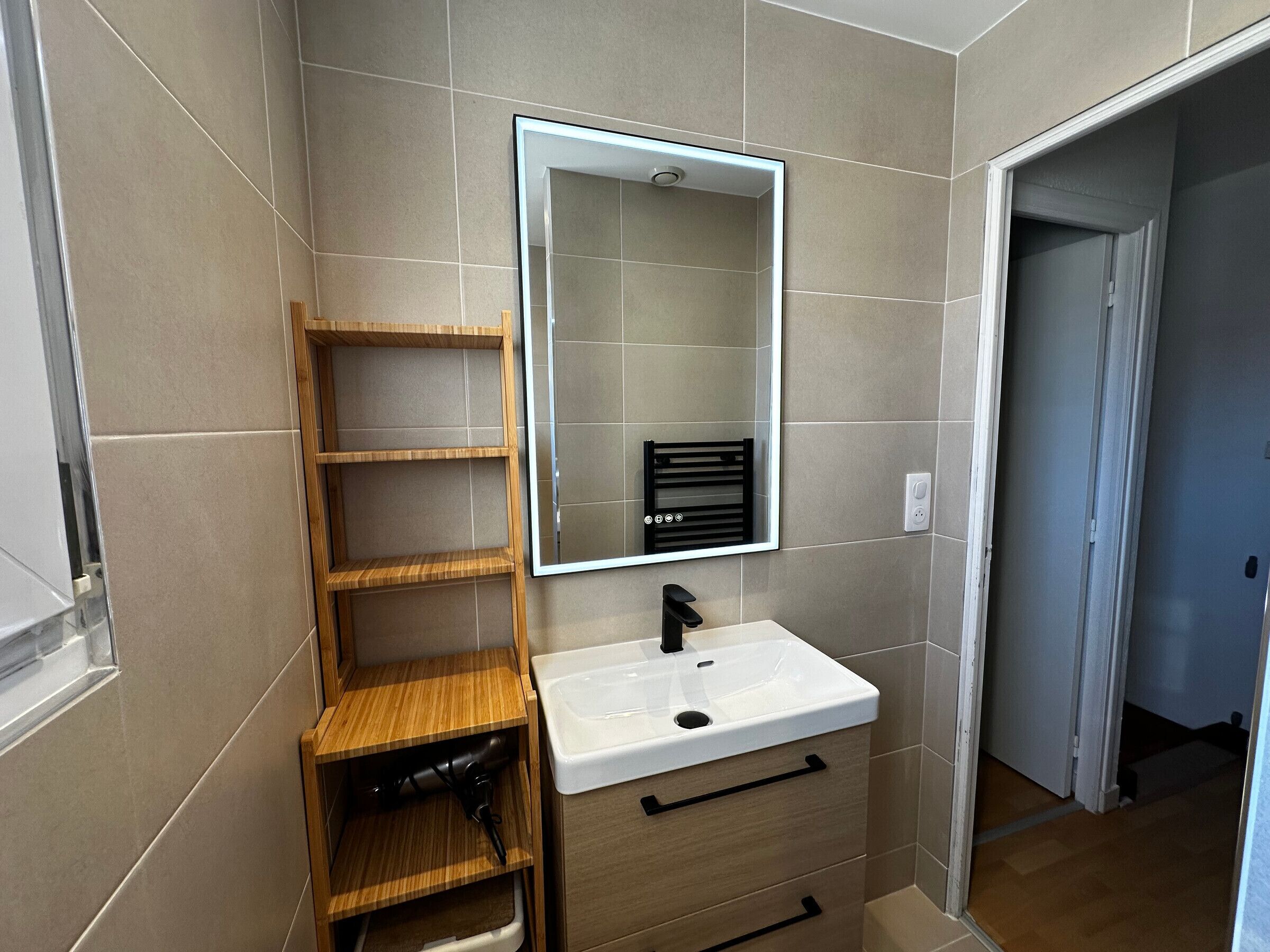 A bathroom with a mirror, a sink, and a wooden shelf unit.