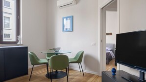 Un appartement moderne comprenant un coin repas, un téléviseur et une chambre à coucher visible à travers une porte ouverte.