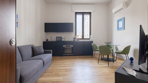 Un espace de vie compact comprenant un canapé, une table à manger avec des chaises, un coin cuisine et un téléviseur.