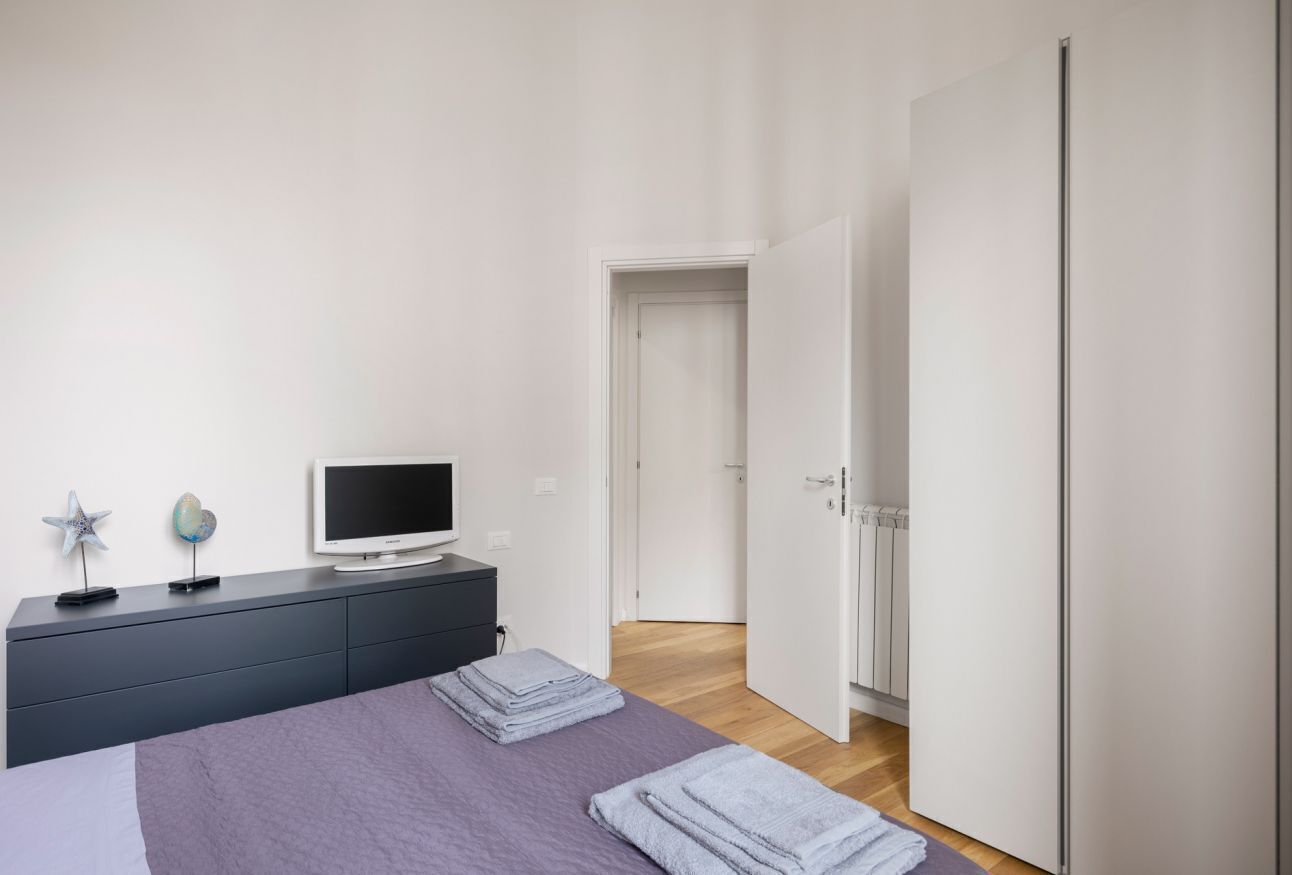 Een slaapkamer met een bed, een televisie op een dressoir en een kledingkast.