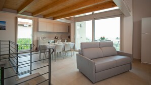 A modern living room with a sofa, dining area, kitchen, and a balcony with a view.