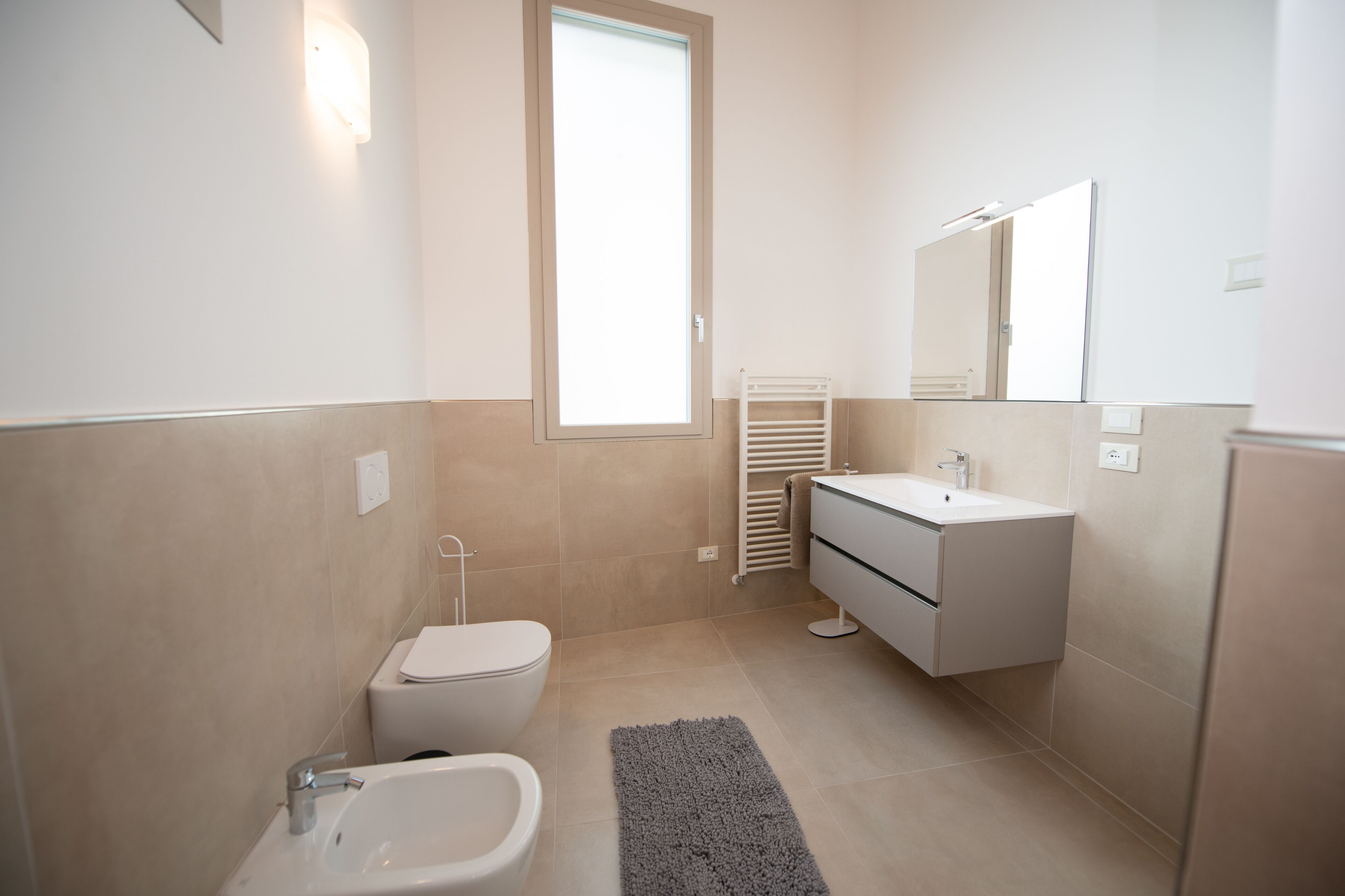 A modern bathroom with a toilet, bidet, sink, and mirror.