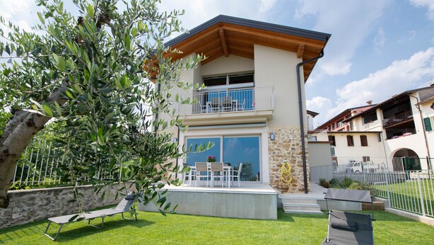 A two-story house with a balcony, a stone wall, and a grassy lawn.