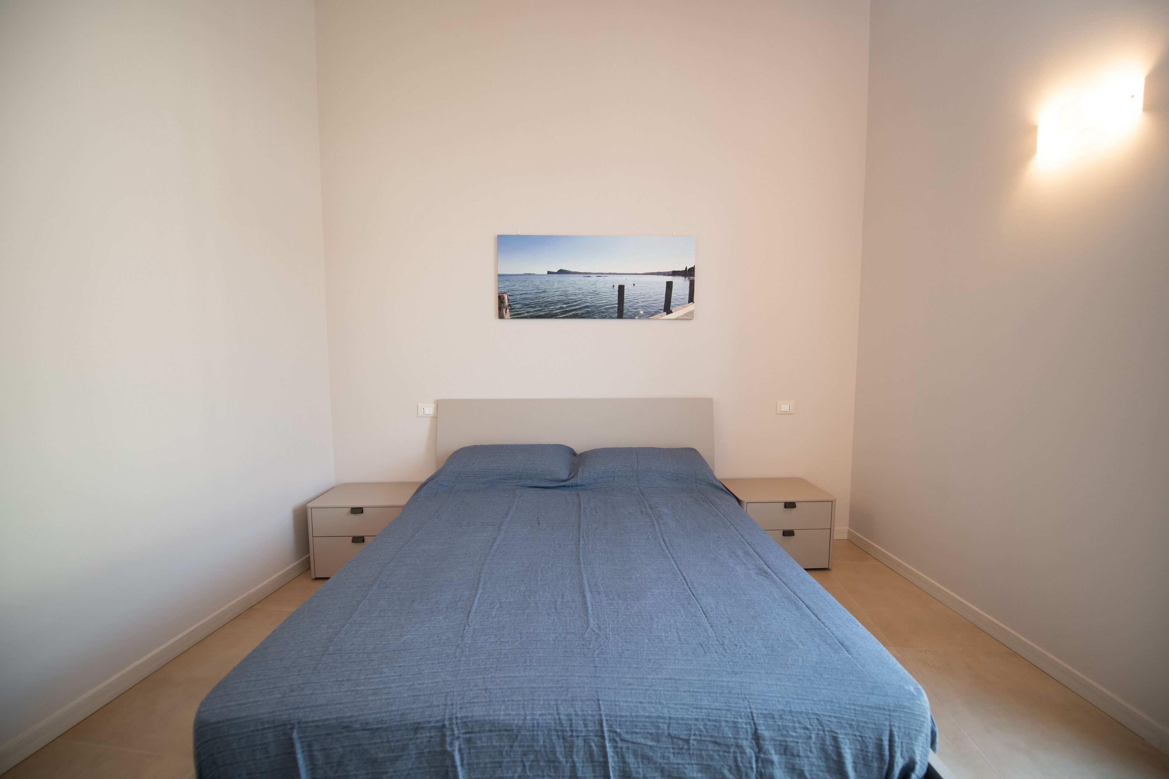 A bedroom with a bed, two bedside tables, a nightstand, and a wall-mounted picture.