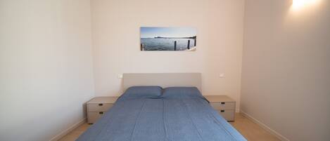 A bedroom with a bed, two bedside tables, a nightstand, and a wall-mounted picture.