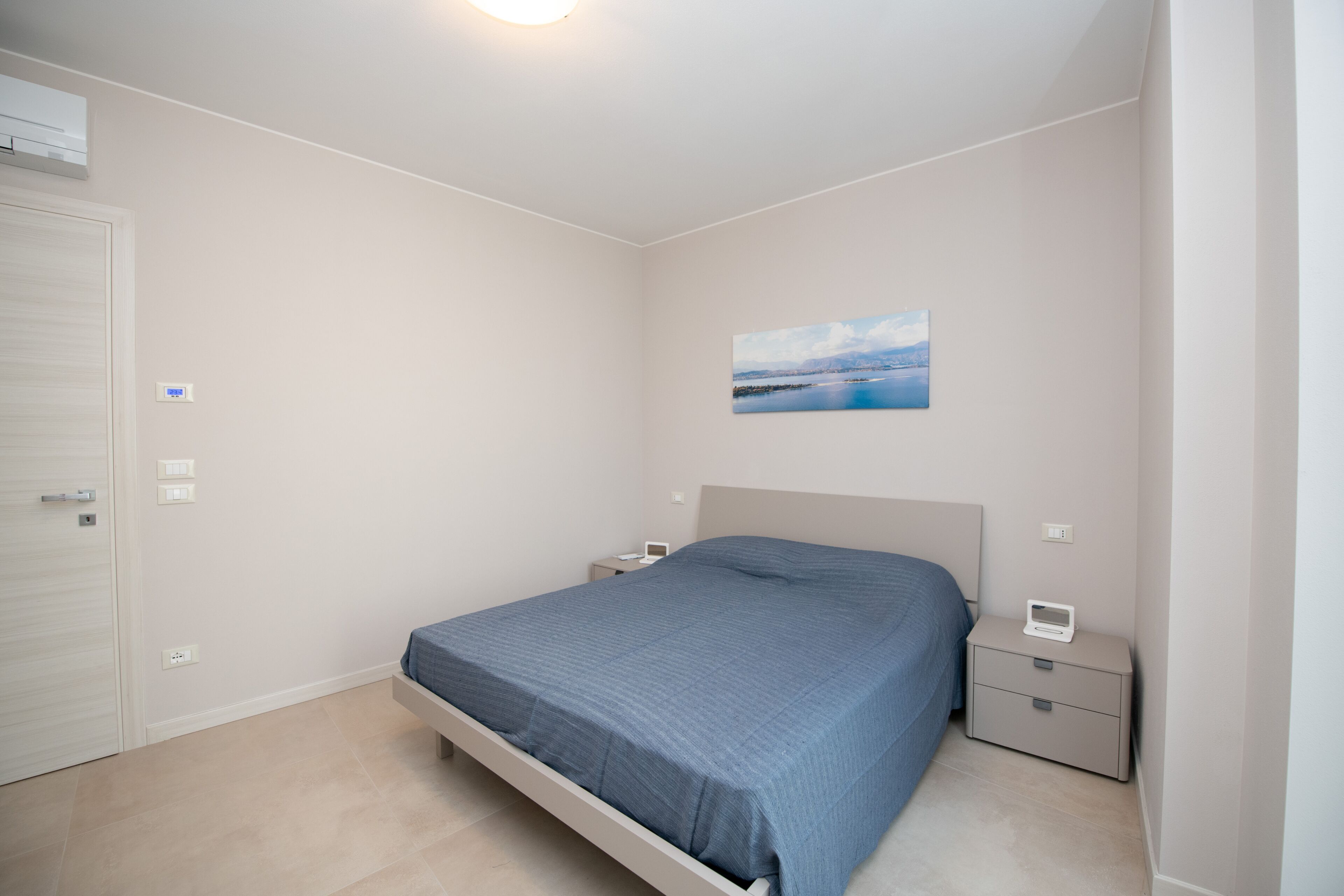 A bedroom with a bed, bedside tables, a nightstand, and a wall-mounted air conditioner.