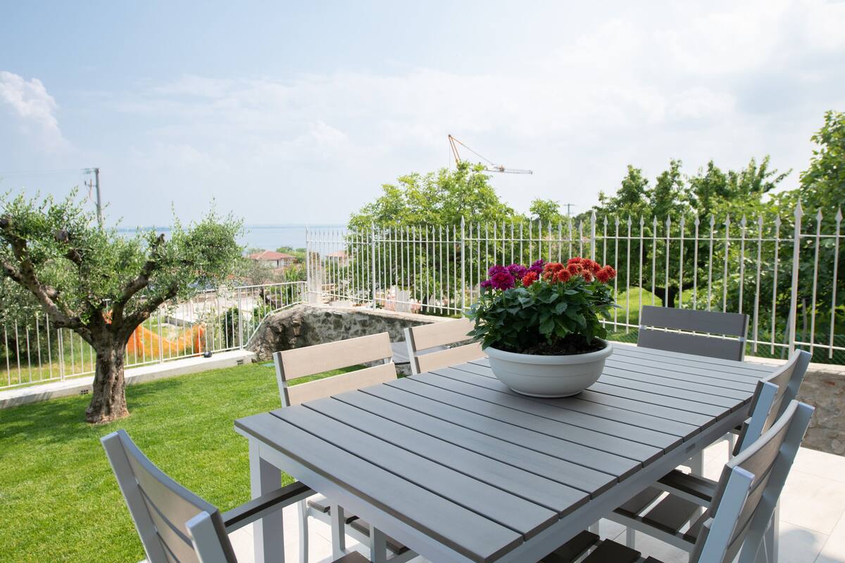 Un patio con una mesa y sillas, una planta en maceta y vista al mar.