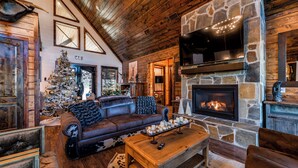 A cozy log cabin interior with a stone fireplace, leather sofa, and a Christmas tree.