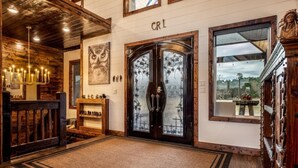 A wooden interior with a large double door, a chandelier, and a view through the door.
