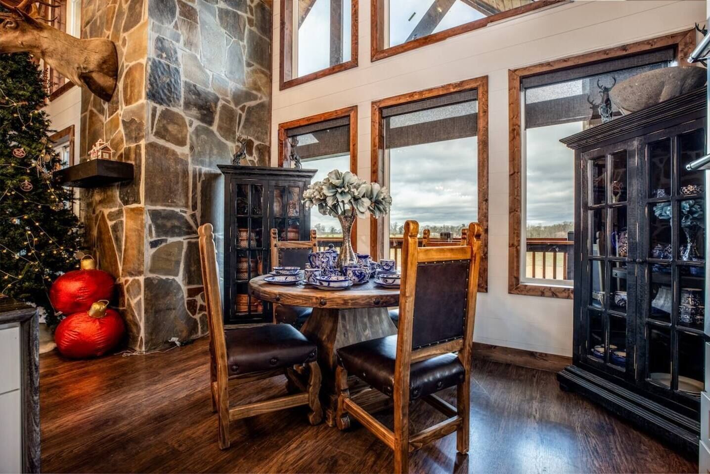 A dining area with a stone wall, a wooden table, and chairs. There is a Christmas tree and ornaments on the left.