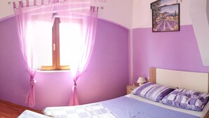 Ein Schlafzimmer mit Bett, Nachttisch, Lampe, Fenster mit Vorhängen und einem Bild an der Wand.