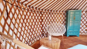 Un interior acogedor con una pared de celosía de madera, una silla de mimbre blanco, una mesita de madera con una lámpara blanca y un armario turquesa.