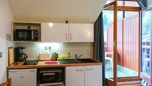 A compact kitchen with a microwave, toaster, coffee maker, and a small oven. There is a wooden table and a sink with a window above it. - Studio with balcony in central Brides-les-Bains, WiFi and parking (Brides-les-Bains)