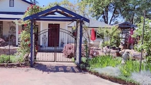 Een poort met een overdekte veranda, een huis met een witte gevel, en een tuin met verschillende planten en een rode parasol.