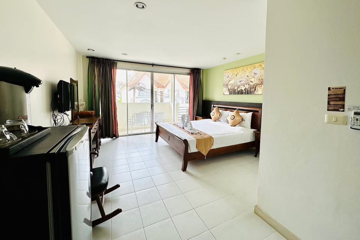 A hotel room with a bed, a desk with a computer, a chair, and a view through a sliding door to the outside.