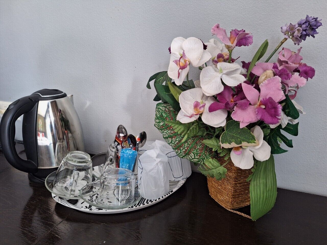 Une table avec un service à thé, une composition florale décorative à base d’orchidées et une bouilloire.