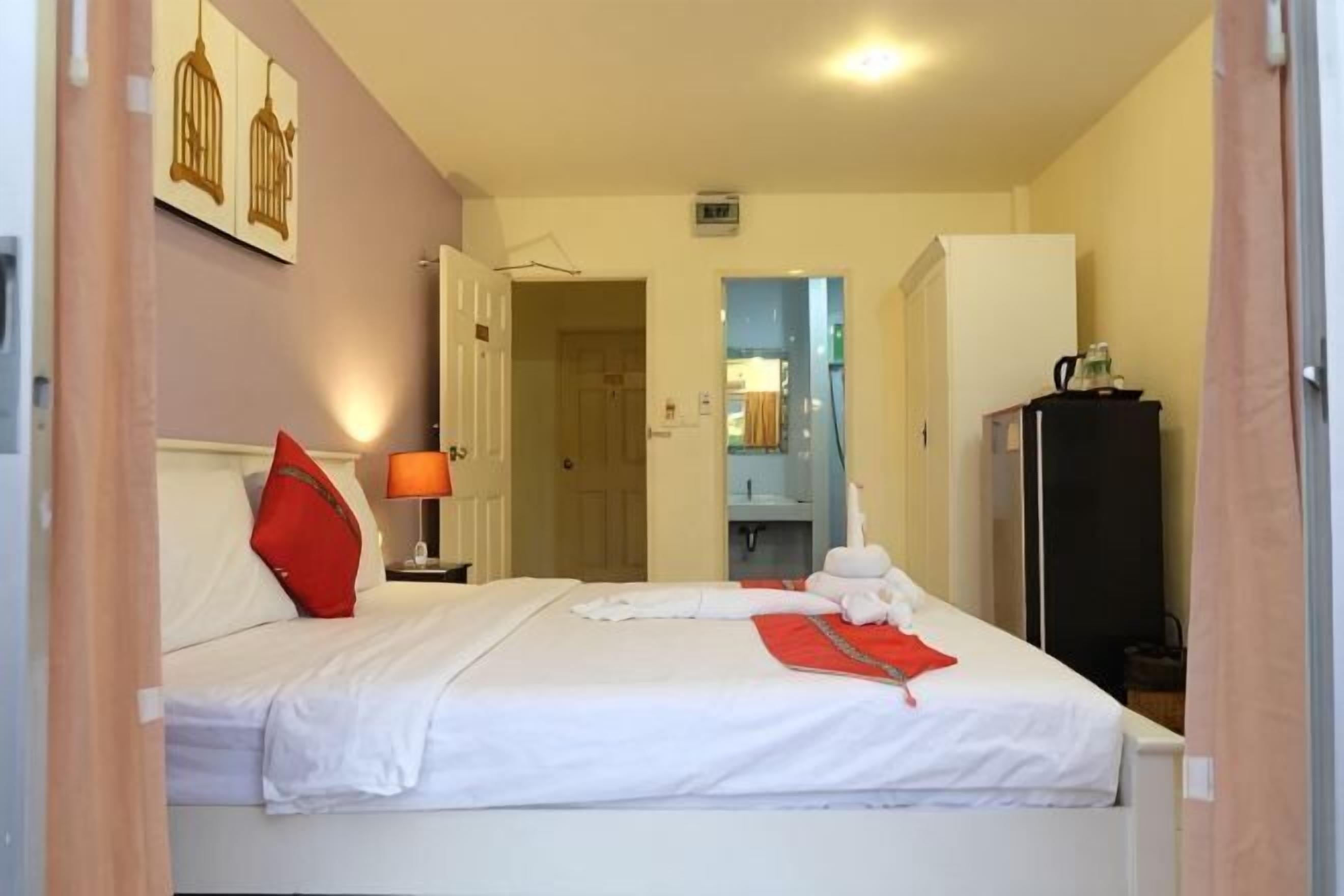 A hotel room with a bed, a nightstand, a lamp, a wardrobe, and a bathroom visible through an open door.