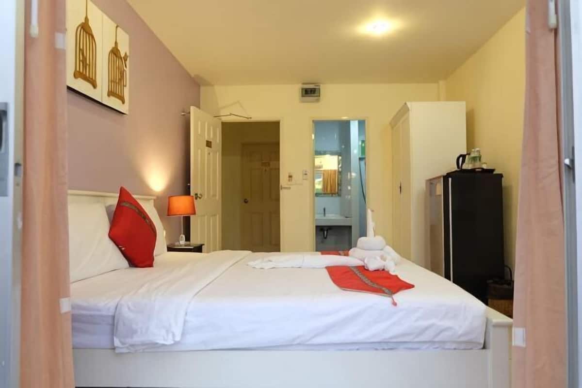 A hotel room with a bed, a nightstand, a lamp, a wardrobe, and a bathroom visible through an open door.