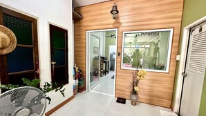 A hallway with a fan, a wooden door, and a mirror reflecting a room with a ceiling fan. - Sea Boss Homestay (Karon)