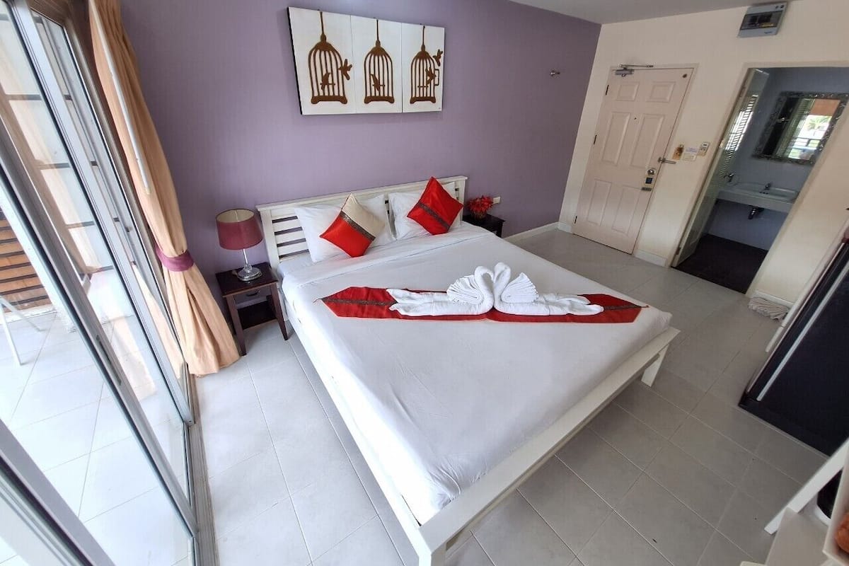 A hotel room with a bed, a nightstand, a lamp, a door, and a window with curtains.