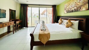 A hotel room with a bed, a desk, a chair, a TV, and a balcony with a view of buildings. - Sea Boss Homestay (Karon)