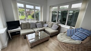 Un salon avec un canapé d’angle, une table basse en verre et un téléviseur posé sur une table blanche.