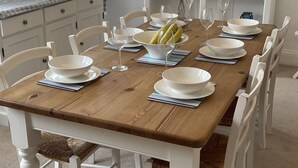 Une salle à manger avec une table en bois dressée pour six personnes, des chaises blanches et un meuble-buffet blanc, de style étagère, agrémenté de décorations maritimes.