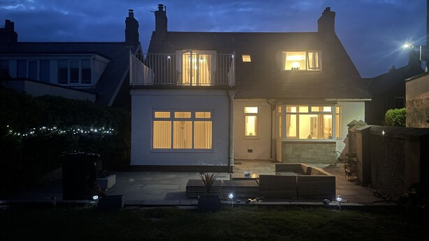 Une maison à deux étages dotée d’un balcon, d’une terrasse avec des sièges et d’une porte d’entrée bien éclairée.