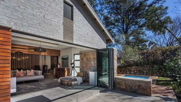 Una casa moderna con fachada de piedra, un portón de cristal que da a un patio y una piscina.