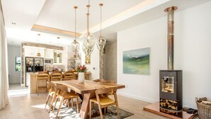 Una cocina moderna con zona de comedor, que incluye una gran mesa de madera, lámparas colgantes y un estufa de leña.