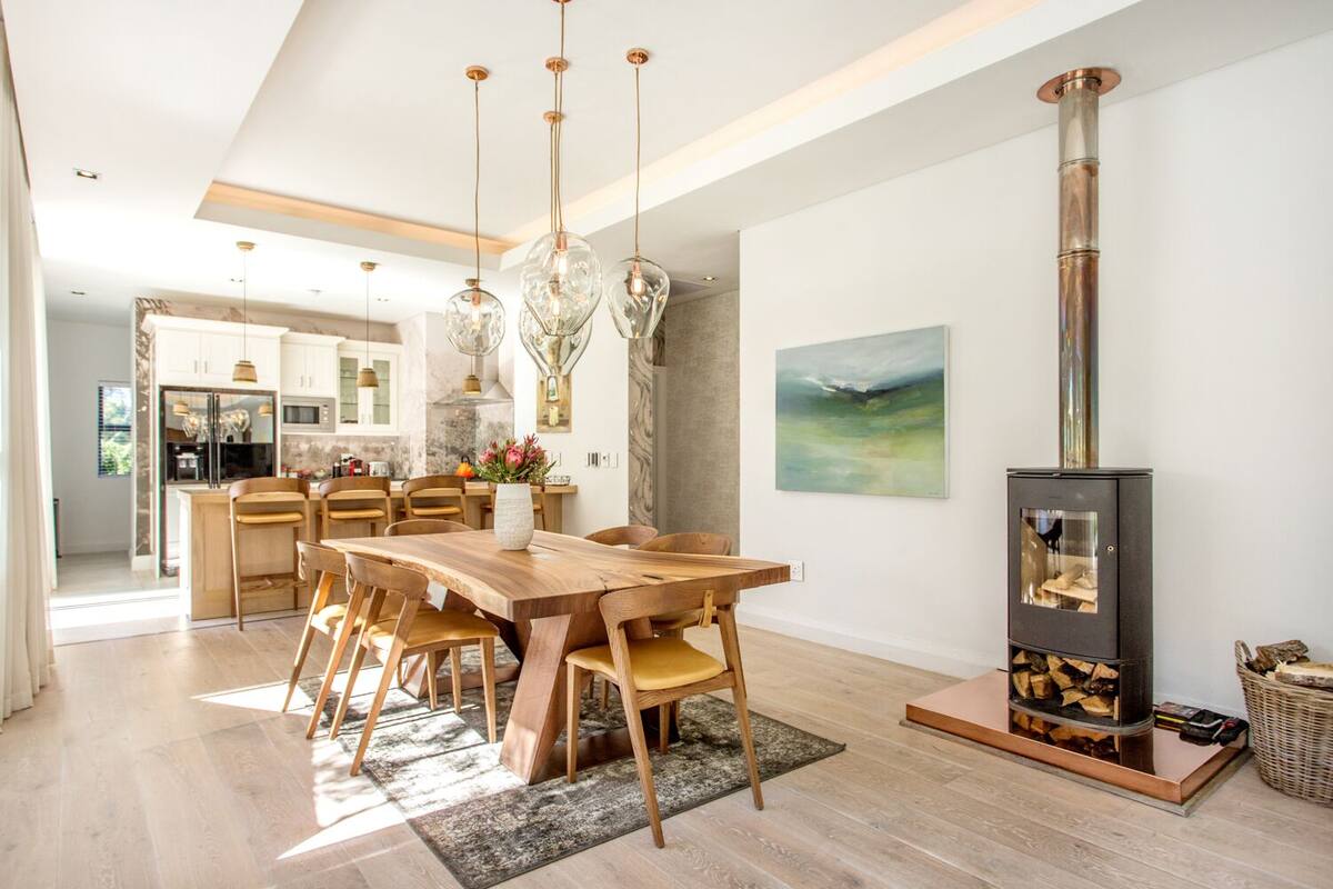 Uma cozinha moderna com área de refeições, apresentando uma grande mesa de madeira, luminárias pendentes e uma lareira a lenha.