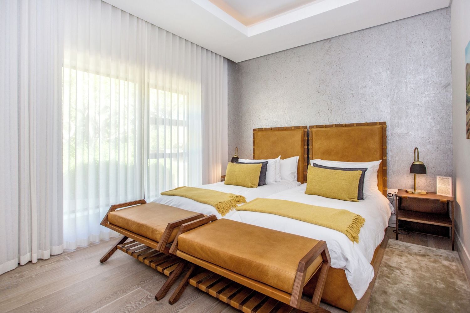 Een moderne hotelkamer met een groot bed, een houten bankje en een nachtkastje met een lamp.