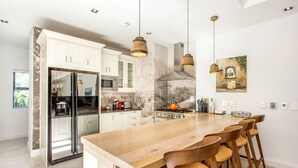 Una cocina moderna con armarios blancos, una isla de madera con taburetes de bar, electrodomésticos de acero inoxidable e iluminación colgante.