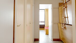 A narrow hallway with white walls, a wooden door on the left, and a wooden ladder on the right.