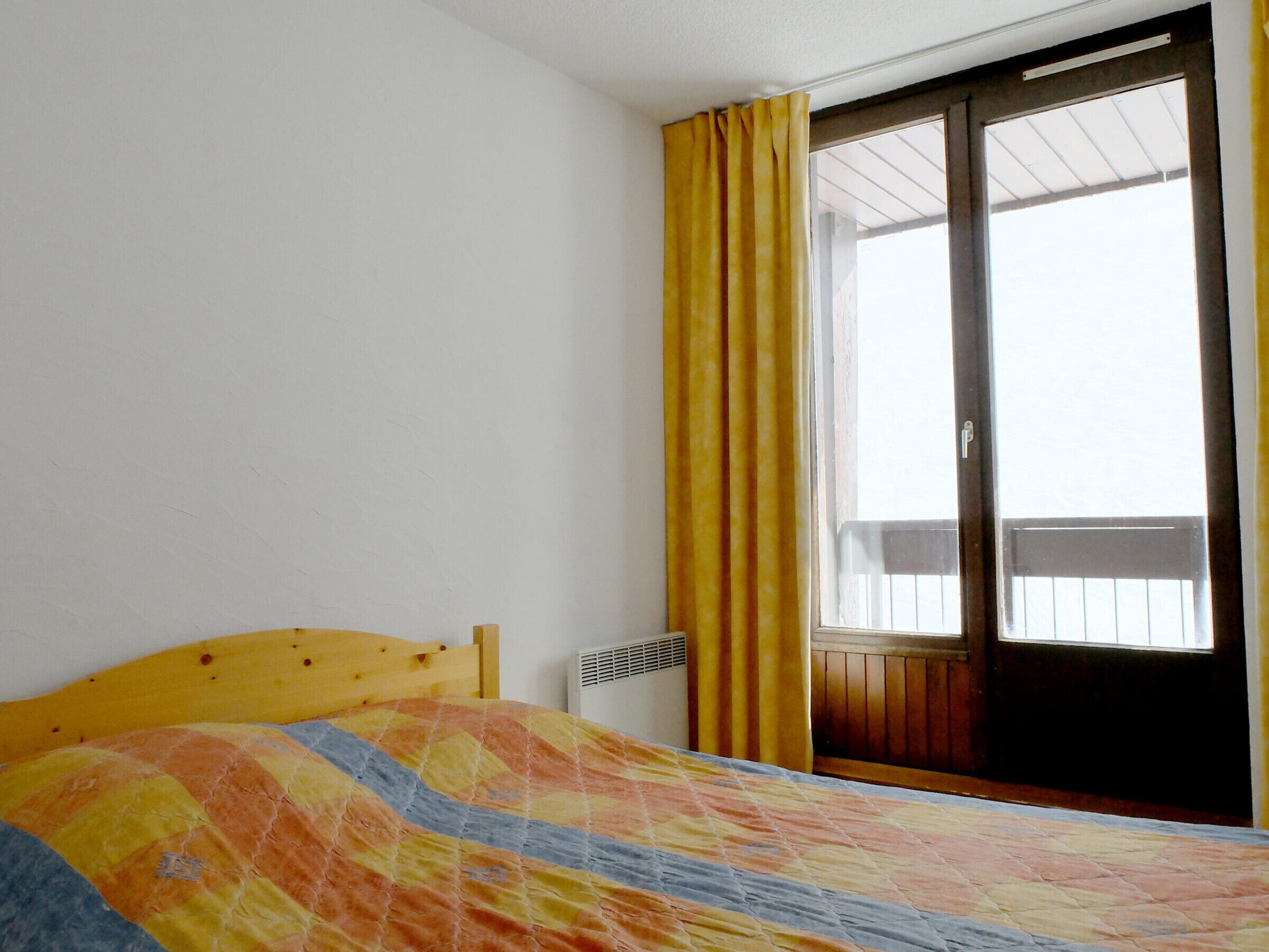 Un dormitorio con cama, ventana con cortinas amarillas y vistas al exterior.