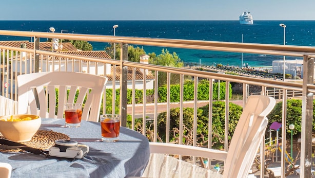 Un balcon avec une table dressée pour deux personnes, donnant sur une zone côtière où l’on aperçoit un navire de croisière au loin.