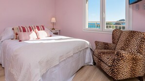 Une chambre à coucher avec un lit, un fauteuil à motifs léopard, une table de chevet, une lampe et une fenêtre donnant sur un beau paysage.