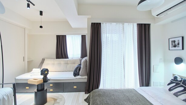 A modern hotel room with a bed, a sofa bed, a desk, and a small table with a vase. - TORA HOTEL Sensoji MOON (Tokyo)