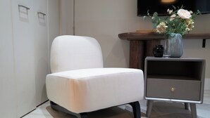 A modern room with a white armchair, a small wooden side table with a vase of flowers, and a flat-screen TV mounted on the wall. - TORA HOTEL Sensoji MOON (Tokyo)