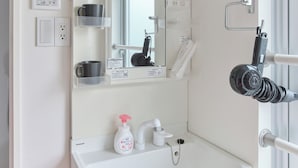 A bathroom with a white sink, mirror, and towel rack. There are toiletries on the sink and a window with a towel hanging on the rack. - TORA HOTEL Sensoji MOON (Tokyo)
