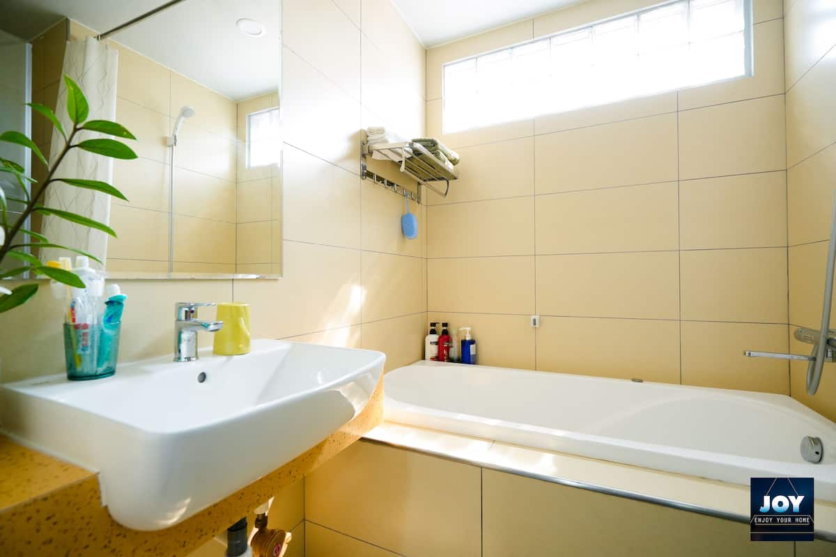A bathroom with a sink, mirror, shower, and bathtub. There are toiletries on the counter and a towel rack above the bathtub.